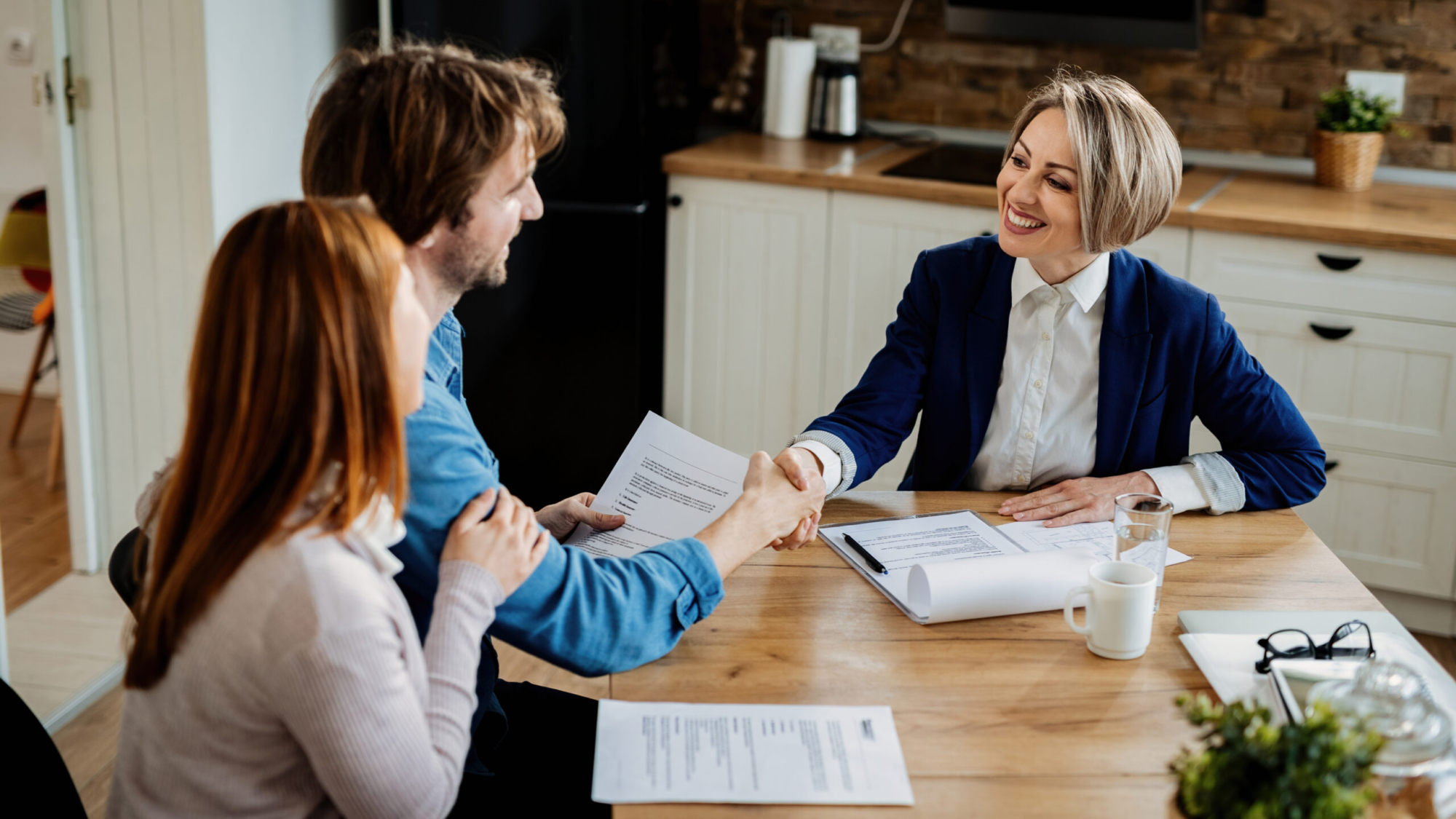 Happy insurance agent shaking hands with young couple after successful meeting.